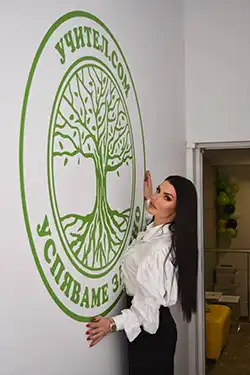 Служителка поставя логото на Учител.com на стената в школата